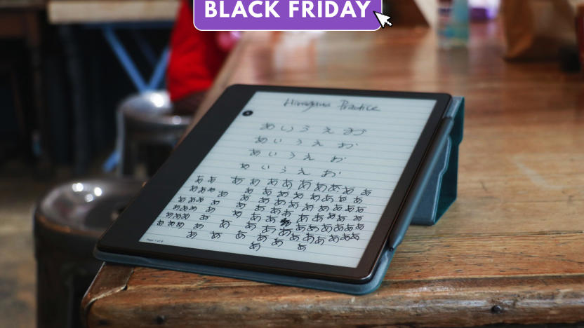 Amazon's Kindle scribe is propped up on a scarred wooden table. Handwritten characters appear on the screen. 