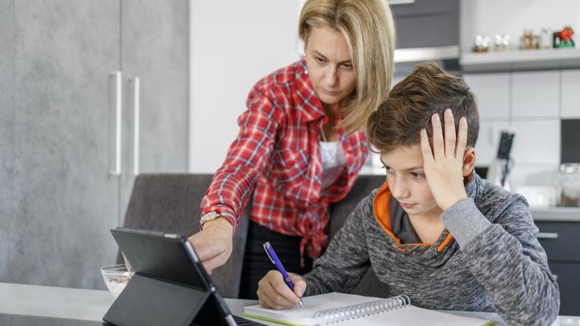 Boy writing homework and mother helping him via digital tablet