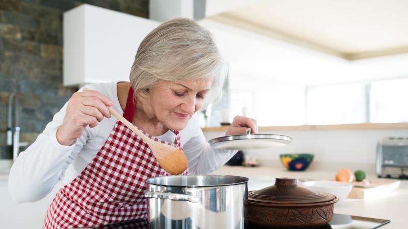 Beautiful senior woman in the kitchen cooking, mixing food in a pot, smelling it.