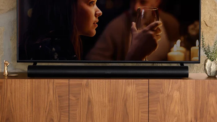 The Sonos Arc sits on a wooden cabinet with a TV above it. 