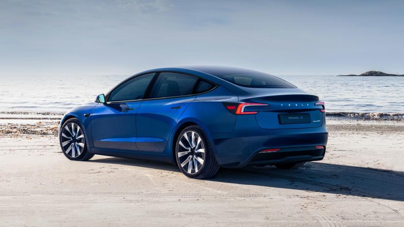 A blue Tesla Model 3 (2024) is parked on a sandy beach right near the edge of where the tide is coming in.