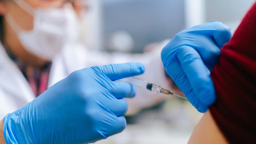 A woman is getting vaccinated by a senior adult doctor in his doctor`s office.