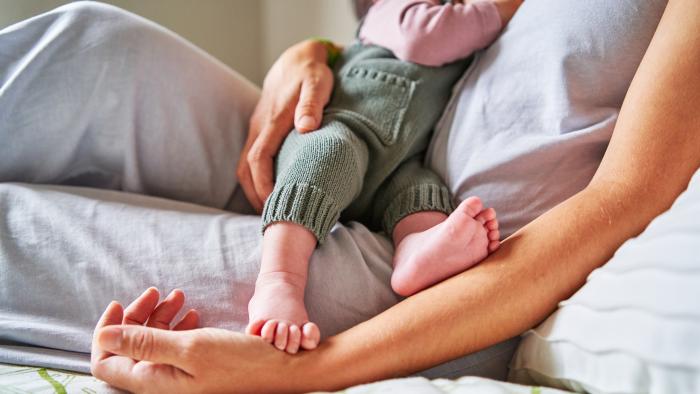 Cropped photo of an unrecognizable baby eating from mother's breast while lying in bed