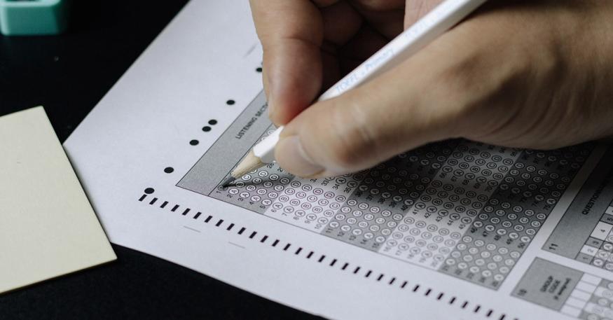 A student uses a pencil to fill a bubble on a paper exam sheet.