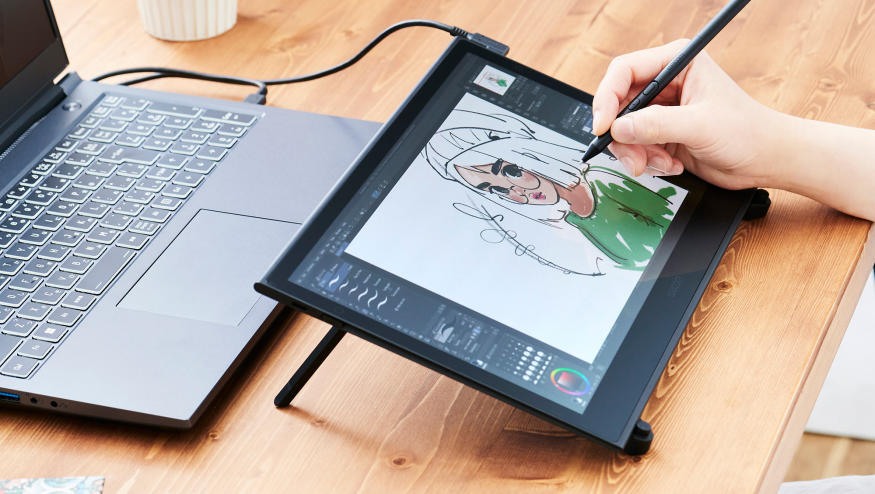 An artist draws on a Wacom Movink pen display that's connected to a black laptop.