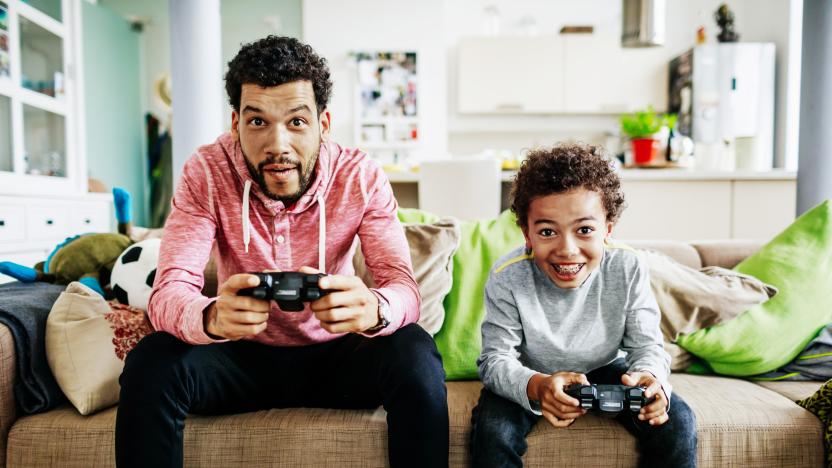 A father and son are concentrating while sitting down at home playing video games together.