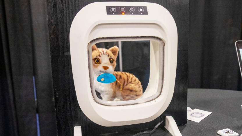 A white Flappie cat door installed in a square of black wood with a stuffed cat and mouse behind it on display at CES 2024.