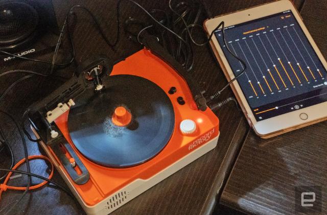 The Teenage Engineering Record Factory vinyl cutter in orange and white seen on a table cluttered with cables, audio gear and speakers.