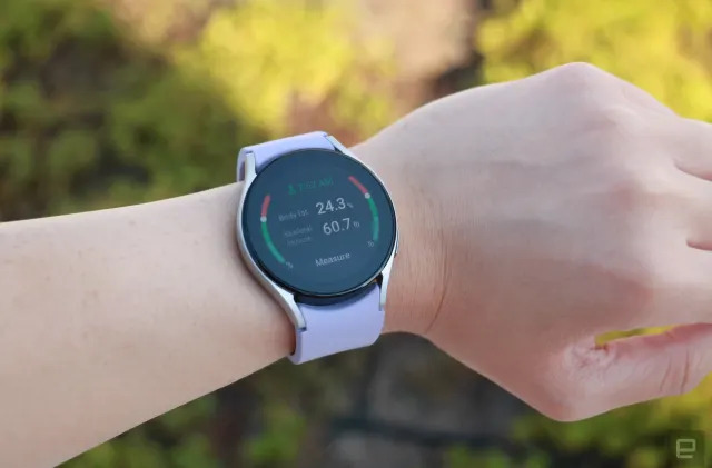 The Samsung Galaxy Watch 5 on a wrist, showing the device's body composition tool with some results displayed. The screen says Body fat is 24.3 percent, while Skeletal Muscle is 60.7 percent. A button at the bottom says "Measure."