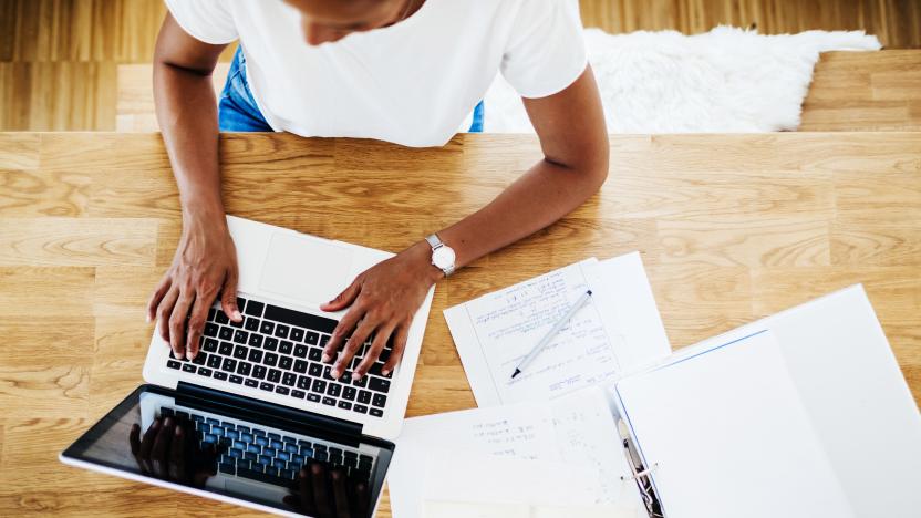 An aerial view of a single mom sitting at her kitchen table, typing on her laptop while working from home.