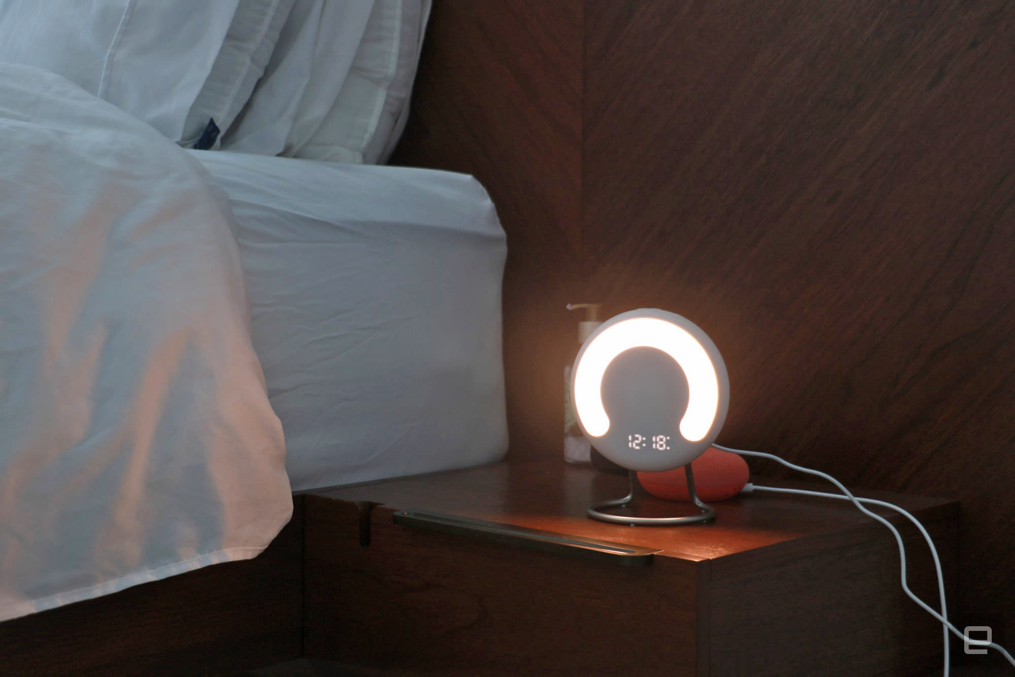 The Amazon Halo Rise on a nightstand in the dark with a the time and a semi-circle lit up on its front.