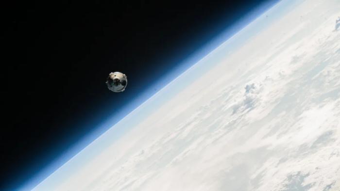 View from the ISS of the Boeing Starliner capsule approaching. Part of Earth, viewed at an angle, is visible behind.