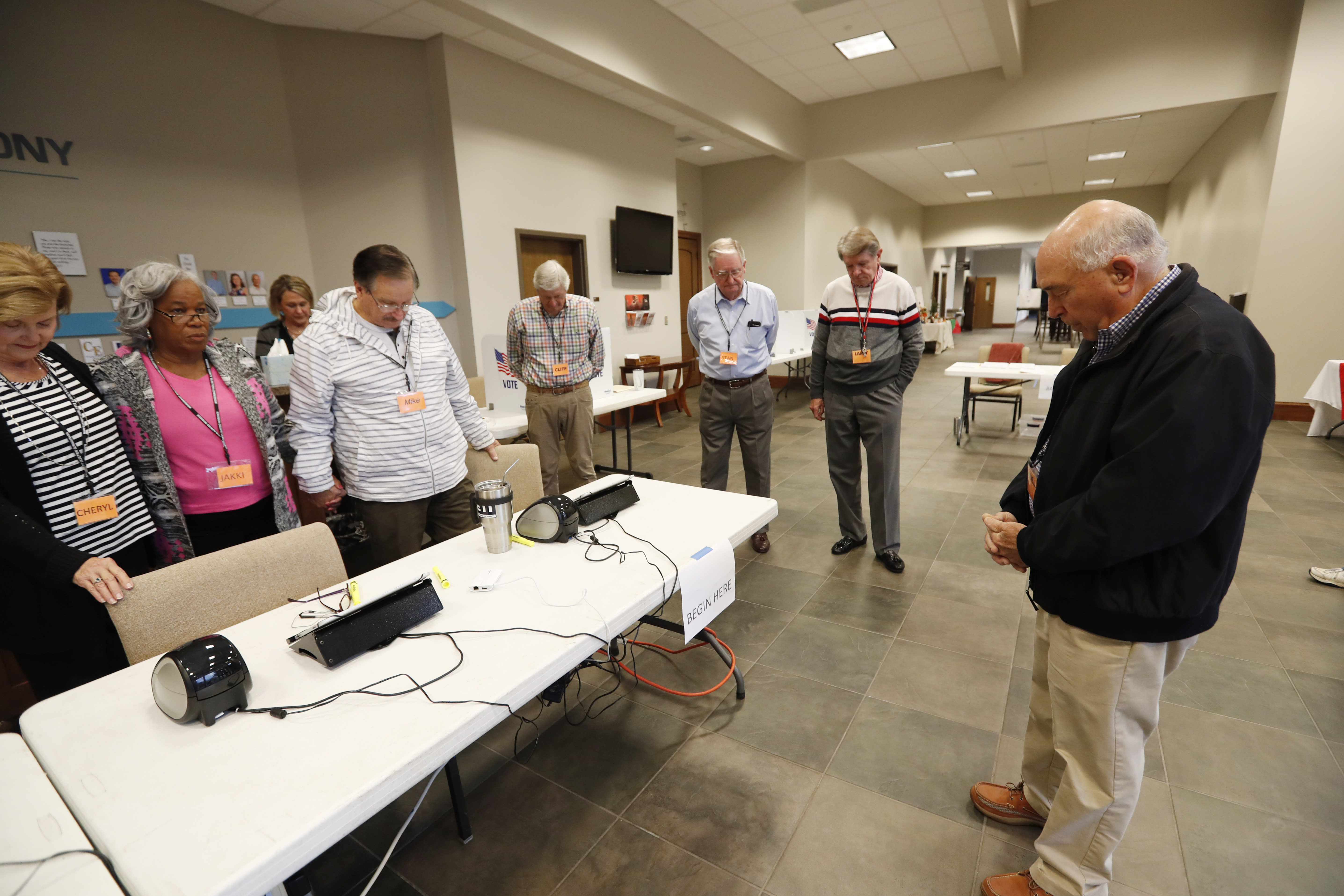 Howell Garner, a Ridgeland, Miss., precinct manager, right, offers a prayer prior to opening the doors to voters, Tuesday, Nov. 5, 2019. Registered voters are having their say in Mississippi's most hotly contested governor's race since 2003 and are also selecting six other statewide officials as well as deciding a host of legislative and local offices. (AP Photo/Rogelio V. Solis)