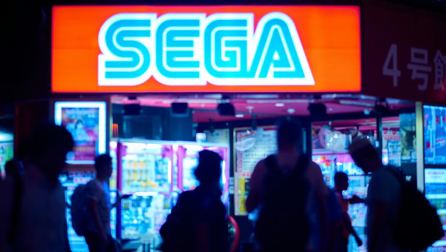 A group of people walk past a Sega sign.