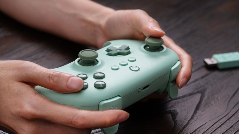 A person holding a lime-green wireless gamepad. A green USB dongle sits behind it on a dark wooden table.