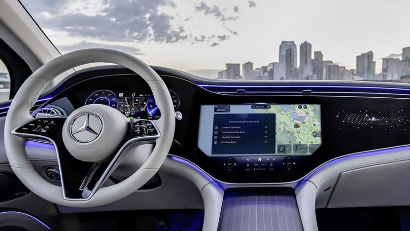 An in-car view of a modern Mercedes interior. The steering wheel is on the left, with main console in the center. In the background is a city skyline.