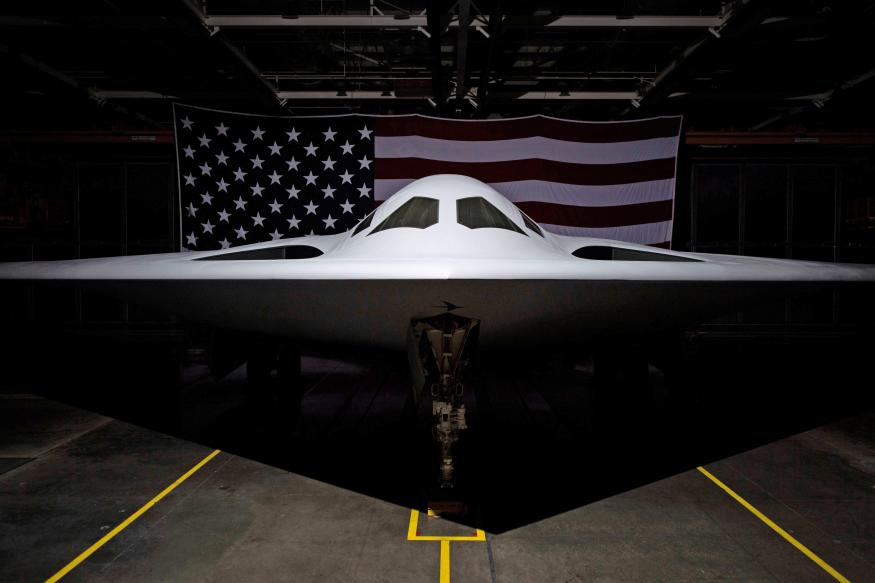 The Northrop Grumman B-21 Raider aircraft photographed in the hangar with an American flag behind it.
