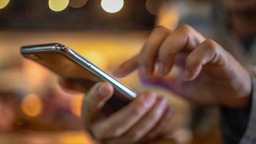 Closeup image of a man holding and using smart phone with coffee cup on wooden table in cafe