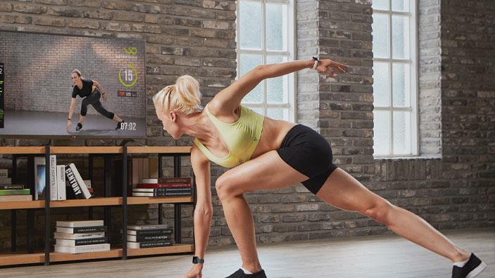 On-demand fitness class Wondercise promotional image showing an at-home exercise person working out in front of a TV. They don't have a lot of furniture, because the pursuit of fitness is more important than a couch.