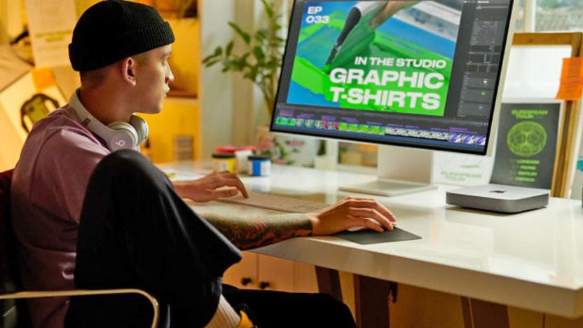 A graphic designer sits at their desk with a Mac Mini clearly visible on the desk top.