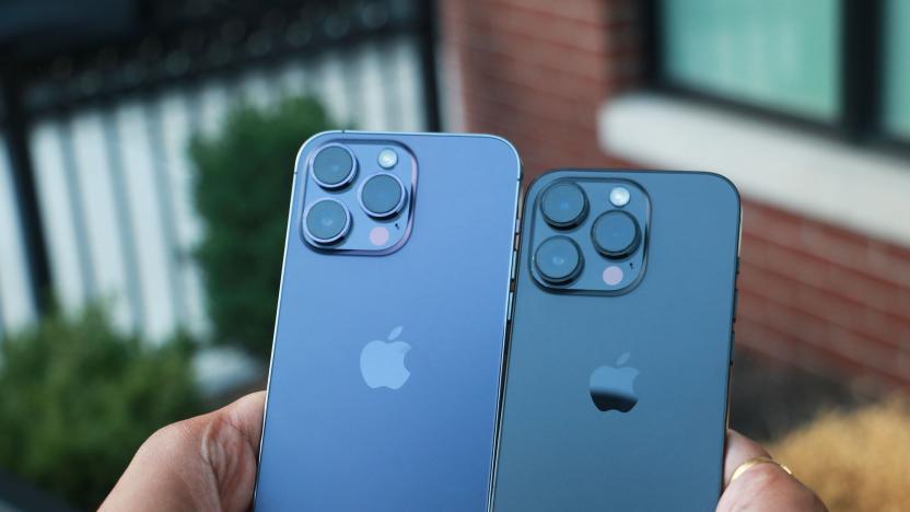 The iPhone 14 Pro Max and iPhone 14 Pro held in two hands, placed next to each other with their rear cameras facing out.