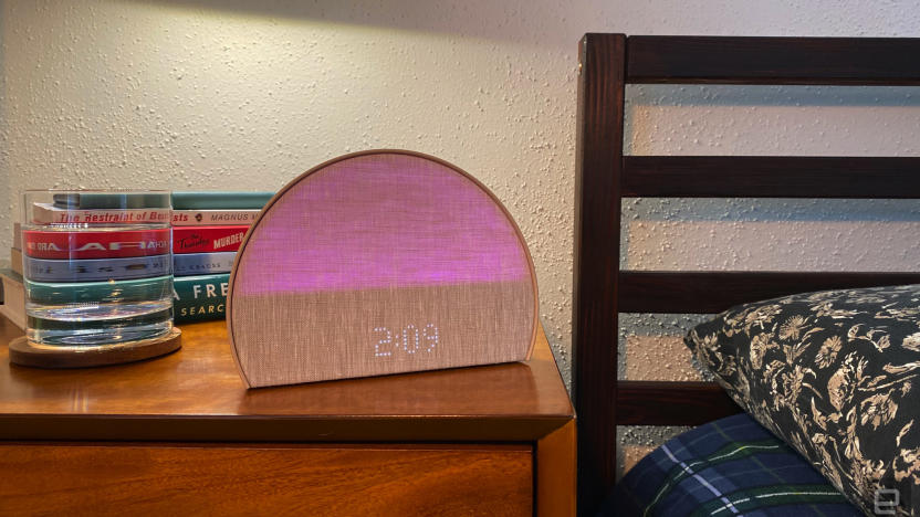 The Hatch Restore 2 sleep machine sits on my bedside table. There's a glass of water and a stack of books in the background. The bed's headboard and pillow are to the right of the image. 