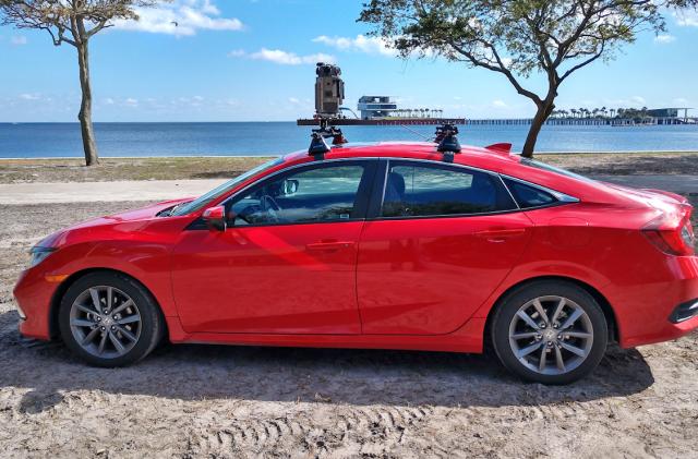 A red car parked on the sand near a waterfront has the new Google Street View camera system mounted on its roof.