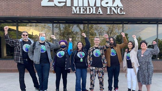 2023 photo of ZeniMax workers standing in a line, raising their fists in unison in front of a ZeniMax Media office.
