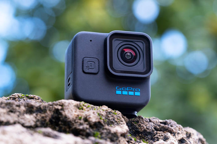 The GoPro Hero 11 Black Mini pictured on a rocky surface in a park with roman-style columns and palm trees in the background.