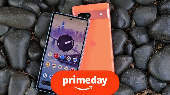 Two orange Google Pixel 7A smartphones sit on a number of black rocks, with one phone facing down and the other facing up with its screen activated.
