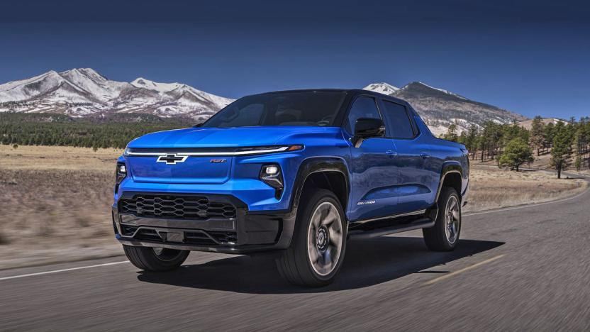 GM marketing photo of the Chevy Silverado EV. The blue truck drives on an open highway with beautiful trees and mountains behind.