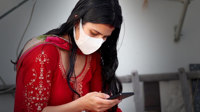 Young Indian women wearing pollution mask against Coronavirus or COVID-19 and she using mobile phone at home.