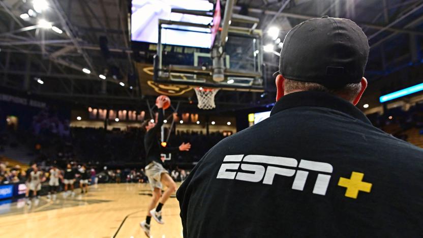 A man with an ESPN+ shirt looks at a basketball player on the court making a layup.
