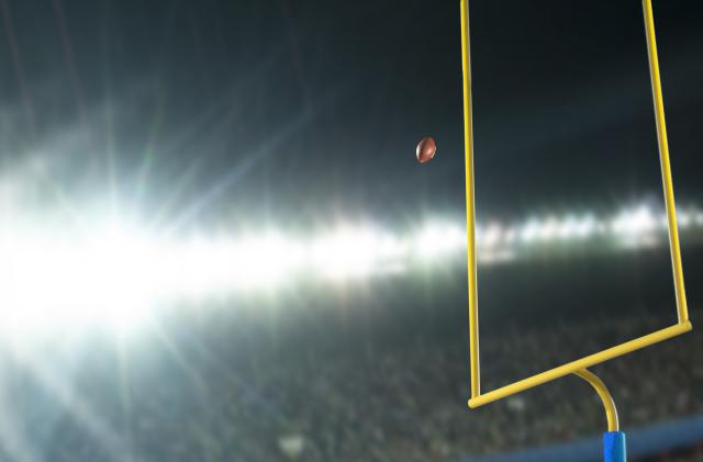 Making a field goal or extra point through the goal post during an American football game at night in stadium with lens flare from the lights.