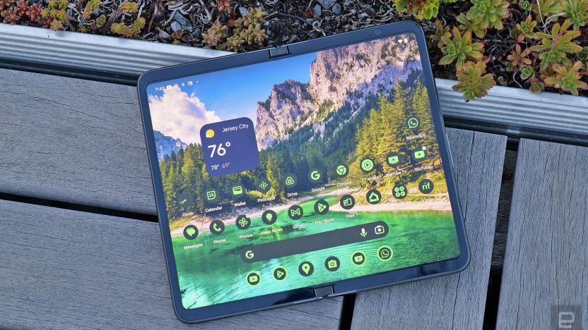 The Google Pixel Fold seen from above in its wide-open tablet-like form as it rests on a bench connected to a planter (small plants are seen in the edge of the shot).