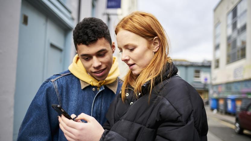 Teenage couple looking at smartphone and smiling, looking for directions or social media while in the street