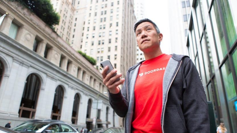 A DoorDash courier (or Dasher) holding a phone as they look into the distance on a city street.