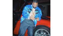 The rapper Drake leaning against a red car, looking at his phone.