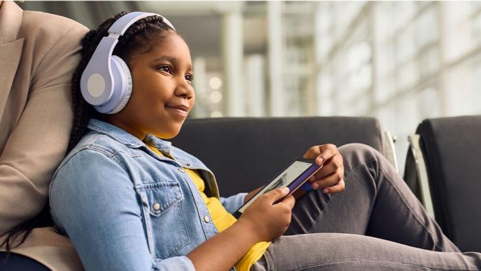 A child wearing headphones listens to an audiobook using a Kindle Paperwhite Kids e-reader,