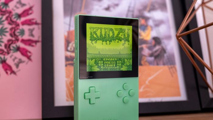 A special edition Analogue Pocket in green is pictured on a shelf with a game onscreen.