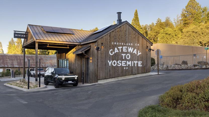 Rivian's Yosemite Charging Outpost pictured showing the outside of the building, which has "Gateway to Yosemite" painted on it in large white letters. A Rivian SUV can be seen parked under its awning