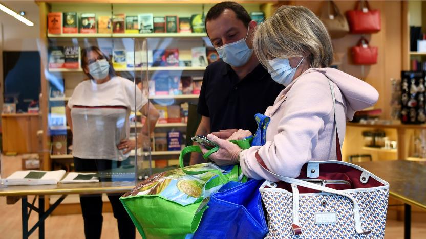 A books seller wearing a face mask looks at a customer's smartphone at a bookstore in Neuilly-sur-Seine, on April 28, 2020, on the 43rd day of a lockdown in France aimed at curbing the spread of the COVID-19 disease, caused by the novel coronavirus. - Bookshops are among the hardest hit by the lockdown measures put in place since March 17. Until stores reopen on May 11, many establishments have already set up a "click & collect" service to provide customers with a book they have ordered. (Photo by FRANCK FIFE / AFP) (Photo by FRANCK FIFE/AFP via Getty Images)