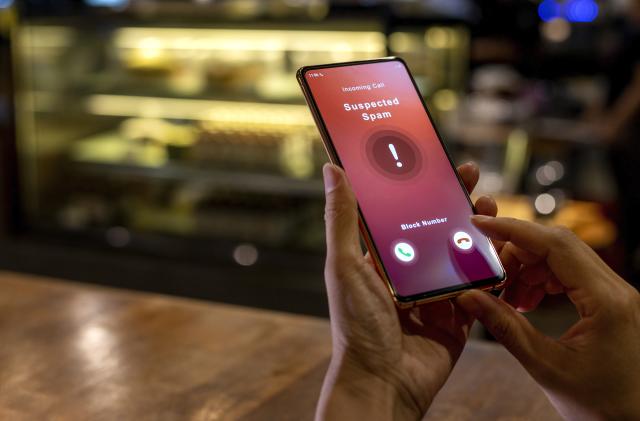 A woman receiving an incoming suspected spam call on her phone. The network provider detect the scam and show warning sign, woman rejects the call.