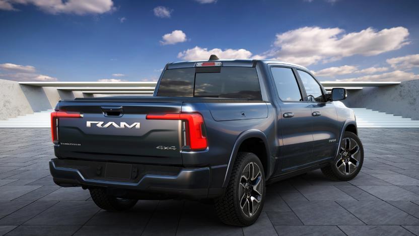 Back view of the upcoming Ram 1500 REV electric truck. It has a dark blue color and is sitting in a modern landscape with tiles and planks in the distance (with a blue sky behind it).