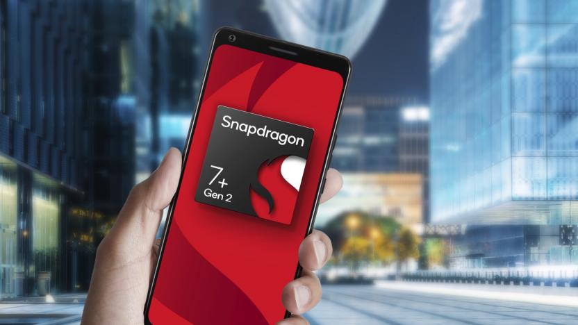 A render of a Snapdragon 7+ Gen 2 chipset displayed on a phone that someone is holding up against a a blurry, modern urban environment.
