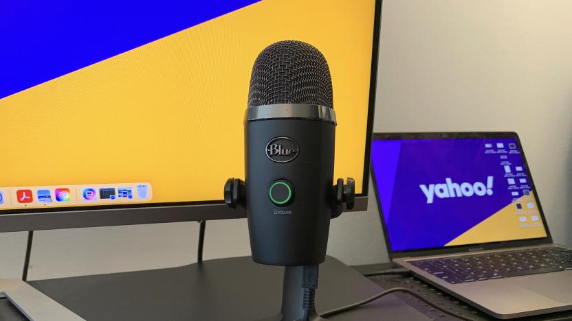 The Blue Yeti Nano microphone on a black desk riser in front of a laptop and a computer monitor.