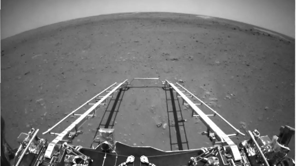 The forward view shows the landscape ahead of the robot as it sits on its landing platform; the rear-looking image reveals Zhurong's solar panels.