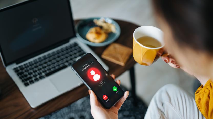 Over the shoulder view of young Asian woman receiving an incoming suspected call from unknown caller on her smartphone and rejecting the call at home. Device screen showing warning sign as detected by the network provider. Phone scam and fraud concept