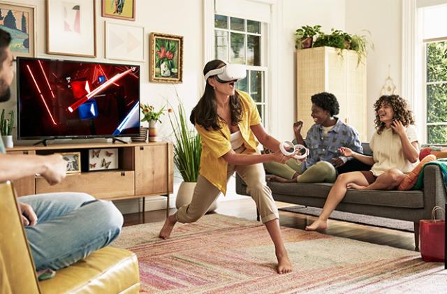 A person uses a Meta Quest 2 headset in a living room as others look on from couches.