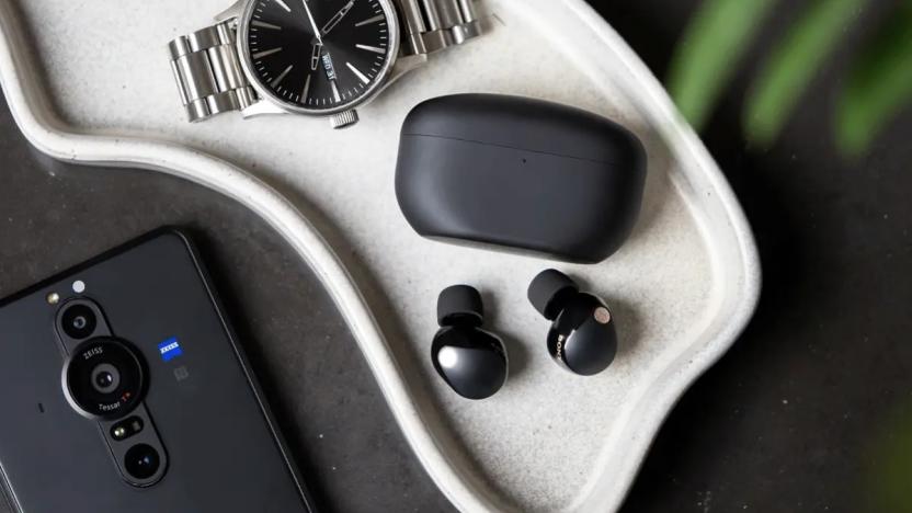 Sony WF-1000XM5 earbuds in black pictured on a tray next to the charging case, a silver watch and a Sony smartphone